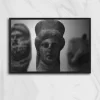 Fotografía análoga en blanco y negro de tres esculturas antiguas de piedra; la figura central, enfocada, muestra un rostro humano con tocado, mientras dos figuras laterales aparecen desenfocadas en primer plano y fondo. Imagen tomada en Udine, Italia, obra Ruinas Udine de Fiorella Angelini, 2018.
