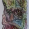 Pintura de Jorge Cabieses-Valdés con una forma orgánica central compuesta por capas translúcidas de verdes, azules y rojos que se mezclan y ondulan sobre una superficie blanca. La imagen presenta texturas densas y relieves de pintura acumulada que generan pequeñas zonas metálicas y rugosas dentro de la composición. Óleo y acrílico sobre tela, 70 x 47 cm, 2019.